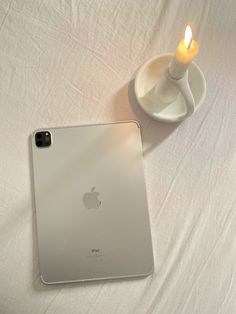 an ipad next to a lit candle on a white sheet with a cup and saucer