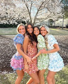 three girls are posing for the camera in front of a tree with white blossoms on it