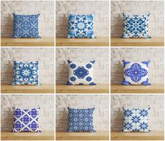 many different blue and white pillows on a wooden shelf in front of a brick wall