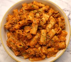 a white bowl filled with pasta and meat covered in sauce on top of a marble counter