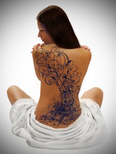 a woman sitting on the ground with her back turned to the camera and tattoos on her body