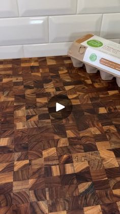 a wooden cutting board with an egg carton in the middle on a kitchen counter