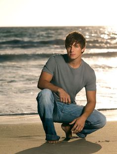 a man kneeling down on the beach next to the ocean