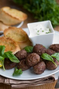 a white plate topped with meatballs next to bread and salad on a wooden table