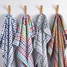 three colorful polka dot towels hanging on a wall next to wooden pegs and clothes pins