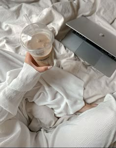 a person laying in bed with a cup of coffee and an apple laptop on their lap