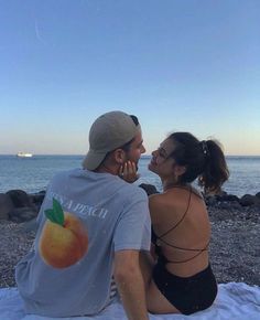 a man and woman sitting on top of a beach next to the ocean looking at each other