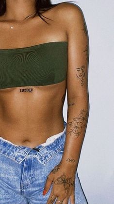 a woman with tattoos on her chest wearing jeans and a green cropped top is standing in front of a white wall