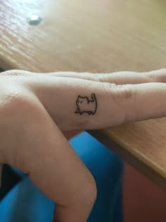 a person's hand with a small cat tattoo on the middle finger and an arrow in the middle