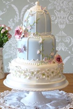 a three tiered wedding cake with flowers on the side and a birdcage