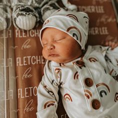 a baby sleeping on top of a blanket wearing a white outfit with brown and orange designs