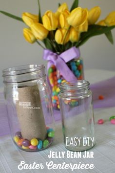 two mason jars filled with jelly beans sit on a table next to a bouquet of yellow tulips