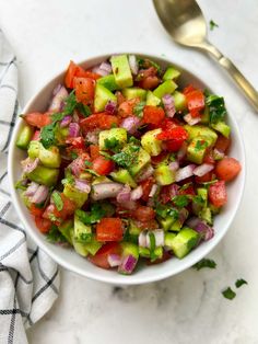 a white bowl filled with cucumber, tomato and onion salad next to a spoon