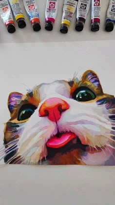 a painting of a cat's face is shown in front of several paint tubes