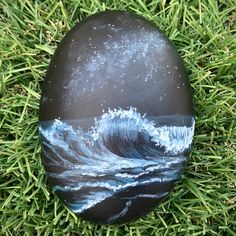 a painted rock sitting in the grass on top of some green grass with water and stars