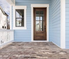 a blue house with a wooden door and white trim on the front porch, next to a brick walkway