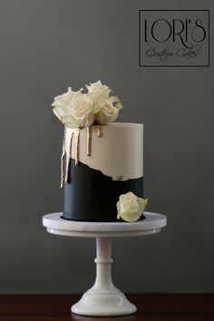 a black and white cake with roses on top is sitting on a pedestal in front of a gray wall