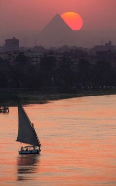 a sailboat in the water at sunset with an island in the distance behind it