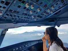 a woman sitting in the cockpit of an airplane looking out at the clouds and mountains