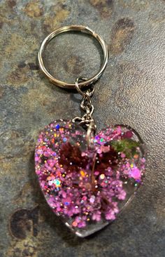 a heart shaped keychain with pink and green glitters on it's side