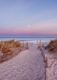 a path leading to the beach with sand and grass on both sides, at sunset