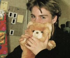 a man holding a teddy bear in front of his face and looking at the camera