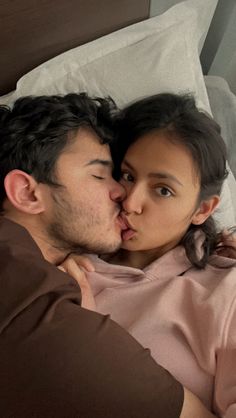 a man and woman laying in bed with their noses close to each other as they kiss