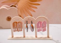 three pairs of earrings are on display in front of a pink flower and white vase