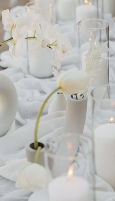 white flowers are in vases on a table with candles and napkins around them