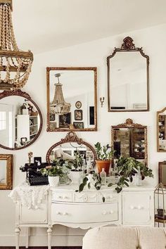 a white dresser topped with lots of mirrors next to a wall filled with framed pictures