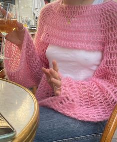 a woman sitting at a table with a glass of wine in her hand and wearing a pink knitted sweater