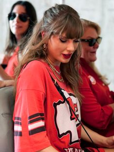 two women in red shirts are looking at a cell phone while another woman looks on