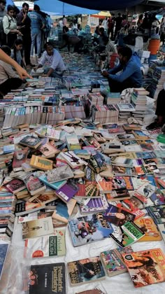 many books are spread out on the ground with people in the background and an umbrella over them