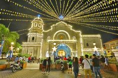 people are walking around in front of a church with christmas lights on the outside and inside