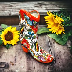 a pair of colorful boots sitting on top of a wooden table next to sunflowers