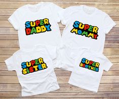 two white shirts with the words super baby and mama printed on them, against a wooden background