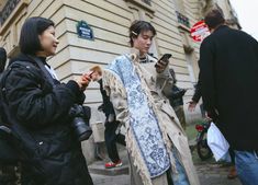 two women standing next to each other in front of a building while looking at their cell phones