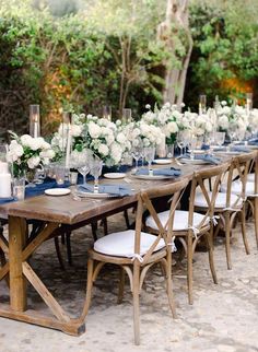 a long wooden table with white flowers and candles on it is set for a formal dinner