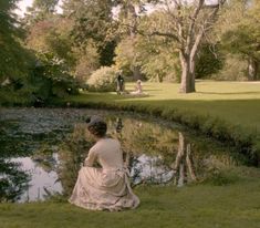 a woman sitting on the grass next to a pond