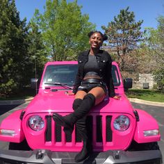 a woman sitting on the hood of a pink jeep