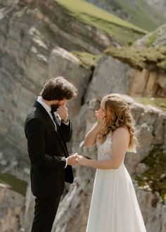 a man and woman standing next to each other in front of a mountain side cliff