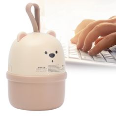 a person typing on a white laptop with a bear shaped mouse attached to the keyboard