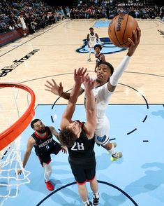 the basketball player is trying to block the ball from going into the hoop while other players look on