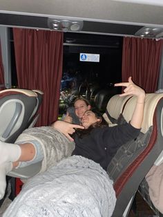 two women sitting in the back of a bus with their hands up and pointing at something