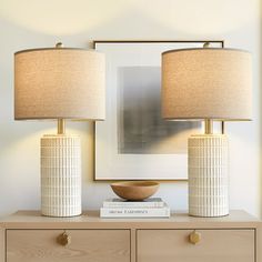 two lamps sitting on top of a dresser next to a framed photograph and a book