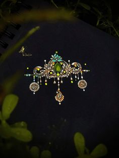 an elaborate brooch with green and yellow beads on it's side, in the dark