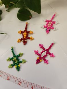 four beaded crosses are shown next to a measuring tape on a table with a plant in the background