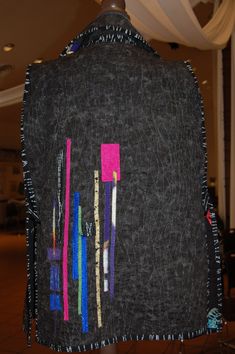 the back of a black jacket with different colored pins and needles on it's side