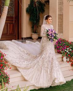 a woman in a wedding dress is standing on the steps with flowers and holding a bouquet