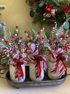 three mason jars filled with candy canes and greenery are sitting on a tray